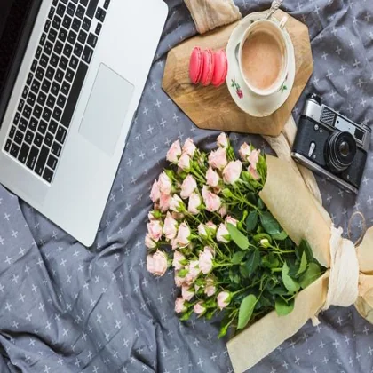 Input photo: a laptop, roses and a cup on a bed